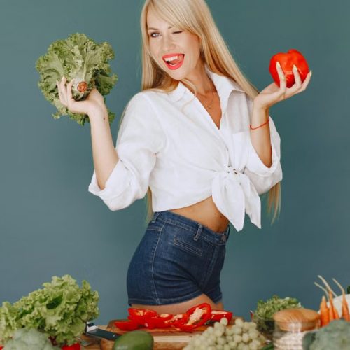 Cheerful woman in white shirt holding lettuce and pepper, celebrating fresh vegetables.